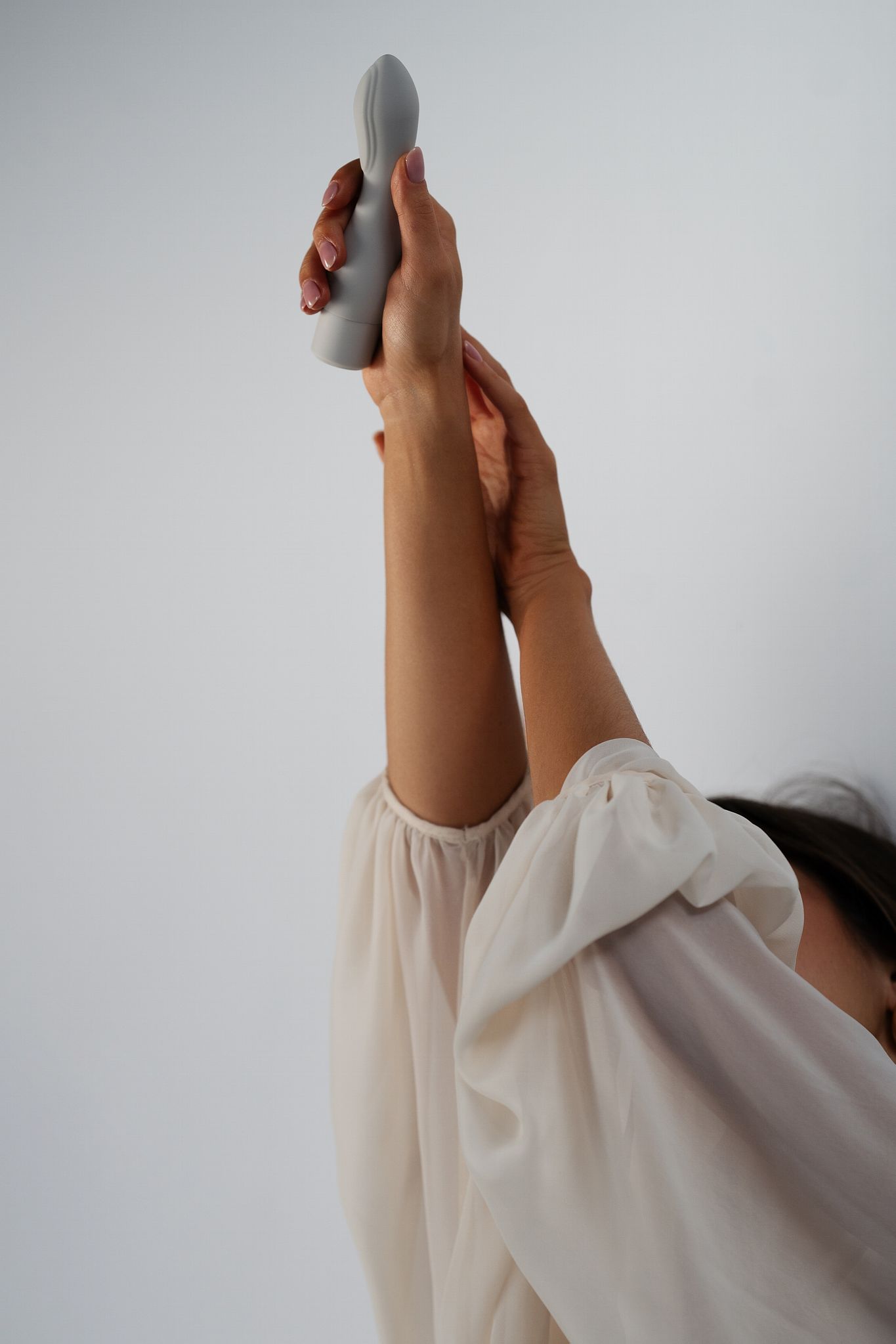 Cima - Naago. Modern external vibrator with sculpted shape held vertically in hand against soft lighting, for self-pleasure