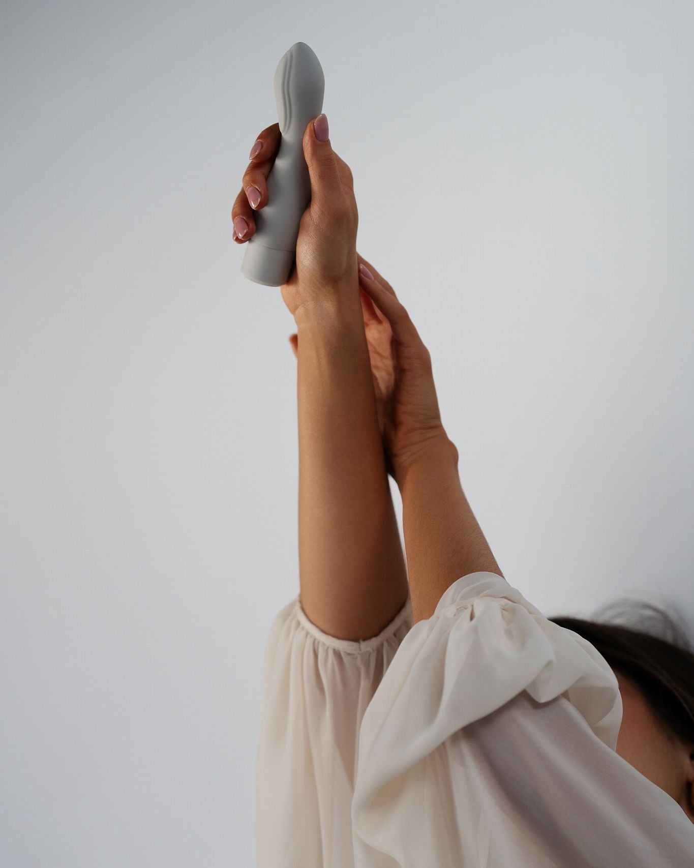 Cima - Naago. Modern external vibrator with sculpted shape held vertically in hand against soft lighting, for self-pleasure