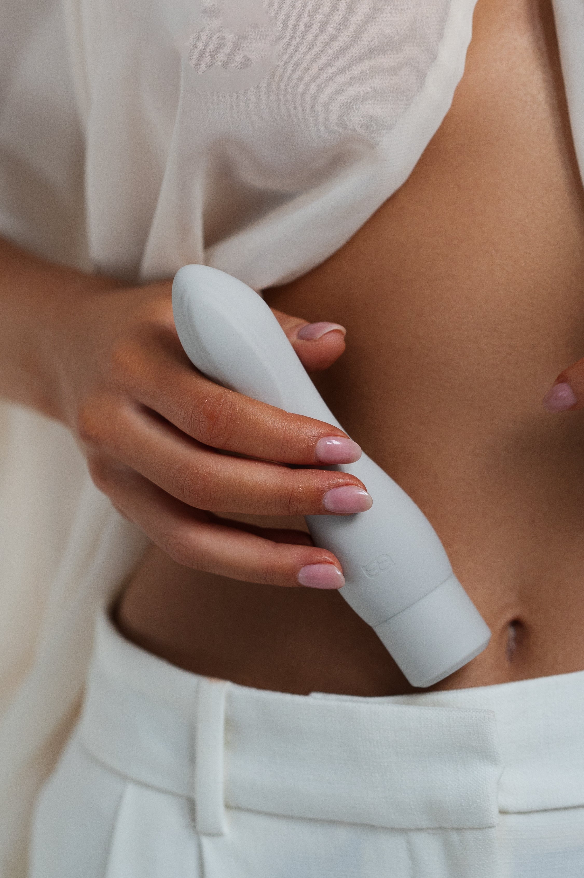 Cima - Naago. Sleek external stimulation sex toy held by hand near bare skin in soft lighting for intimate wellness