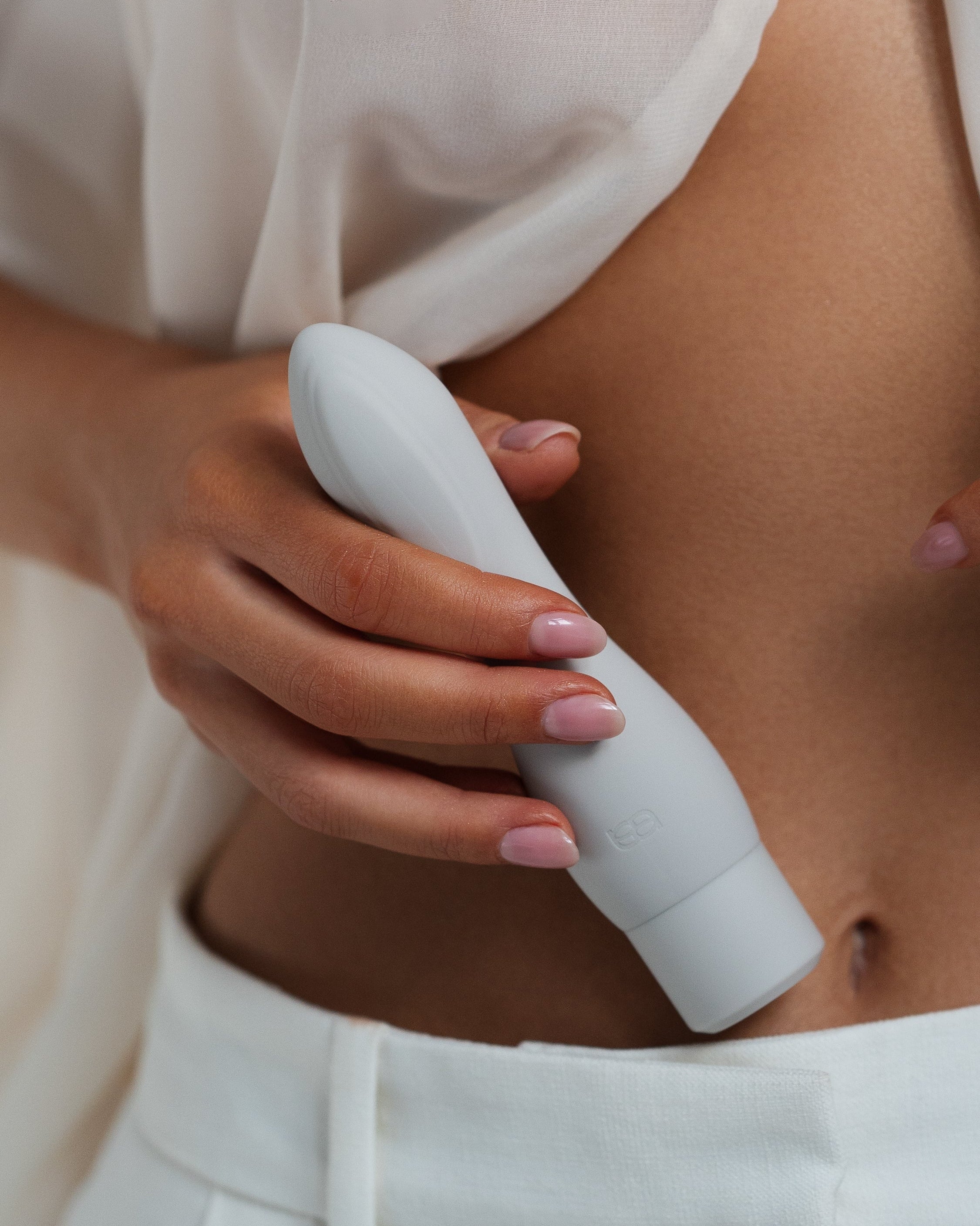 Cima - Naago. Sleek external stimulation sex toy held by hand near bare skin in soft lighting for intimate wellness