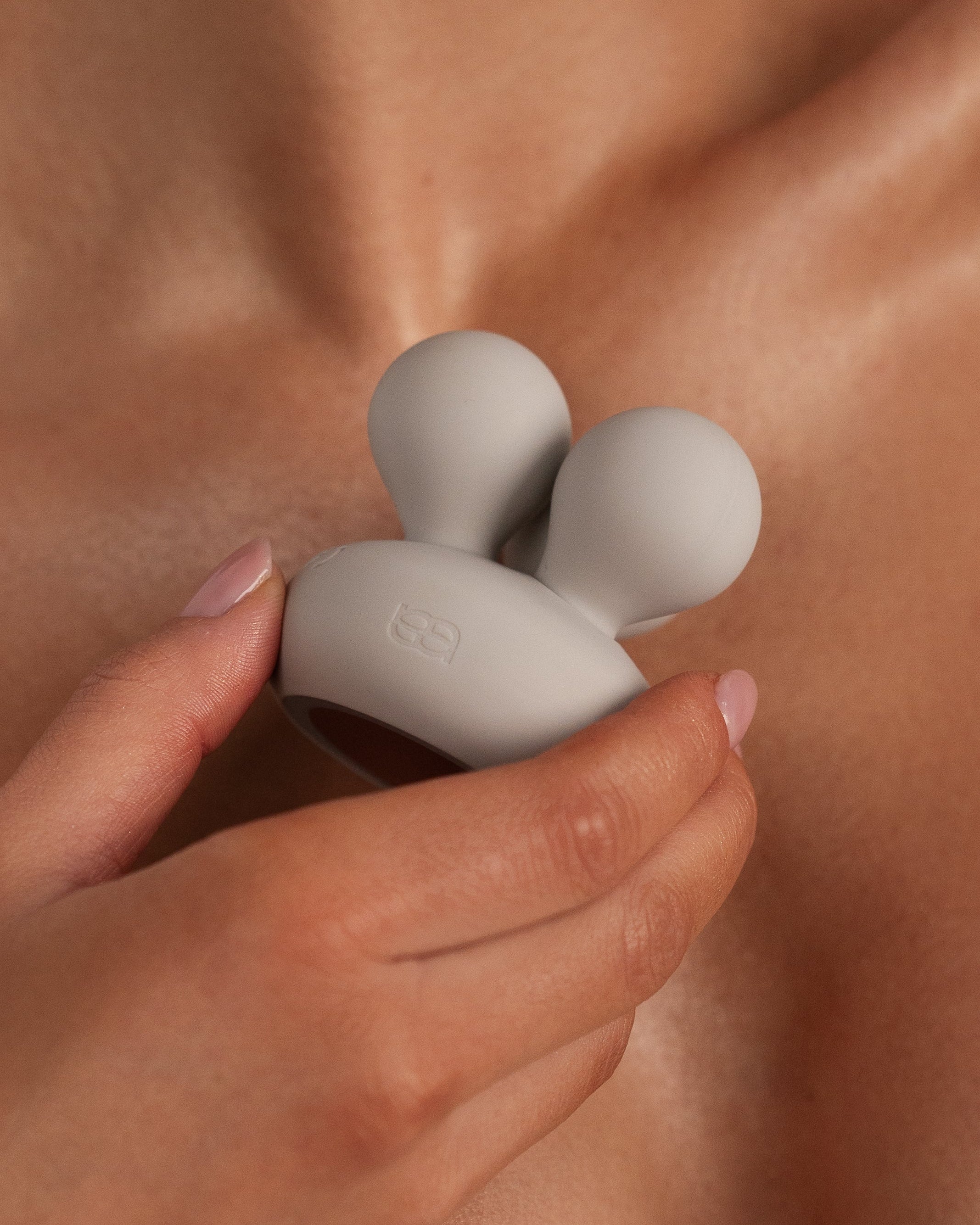 Neve - Naago. Round external vibrator with dual tips held near bare skin for targeted clitoral stimulation and self-care