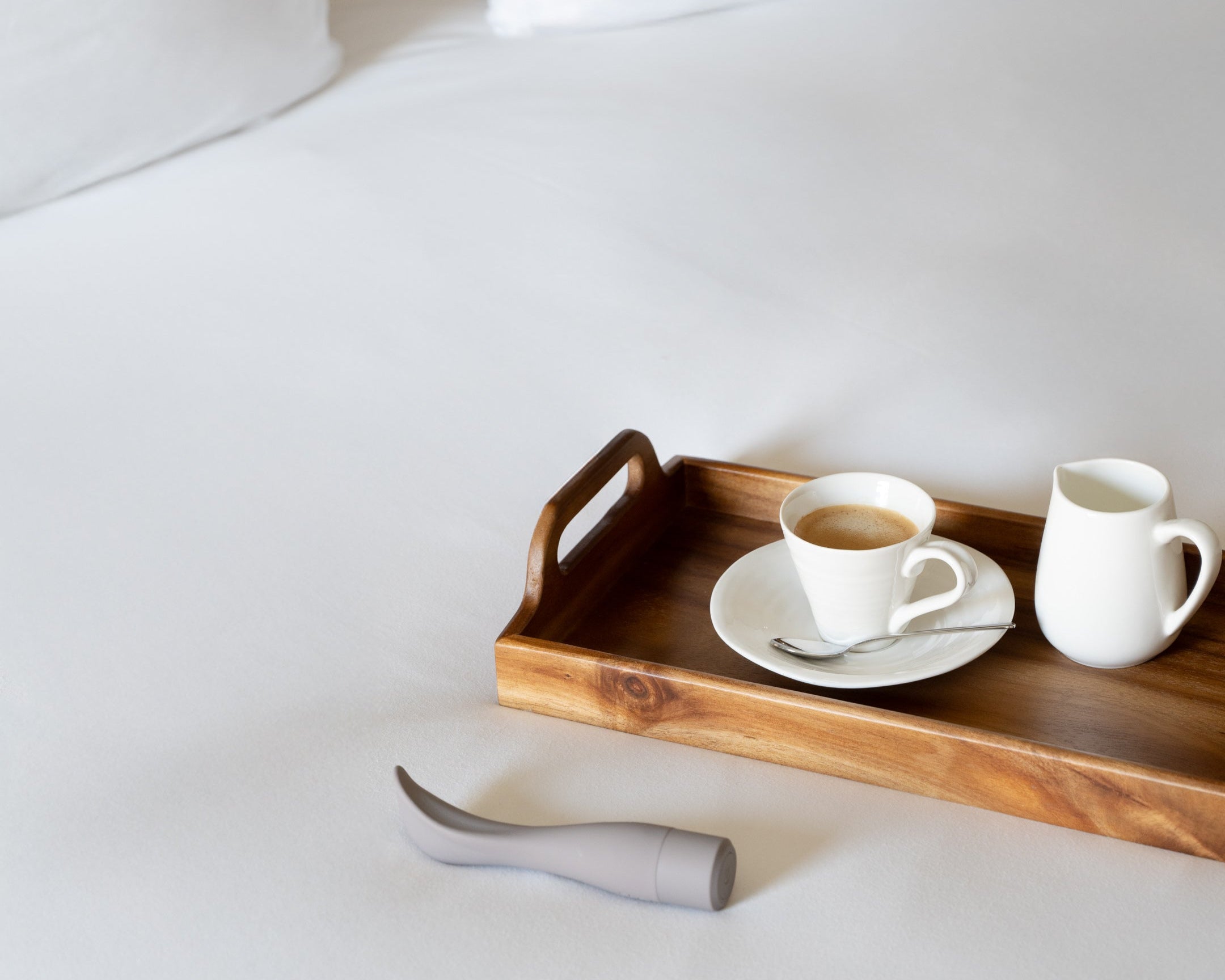 Wooden tray with a cup and saucer on a bed with Naago product next to it